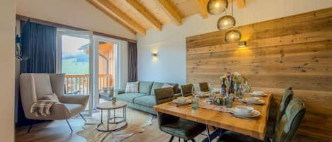 A spacious living area with a wooden ceiling, a dining table set for four, a sofa, and a chair.