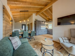 Un vaste espace de vie doté d’un plafond en bois, d’une table à manger avec des chaises et d’une cuisine située au fond de la pièce.