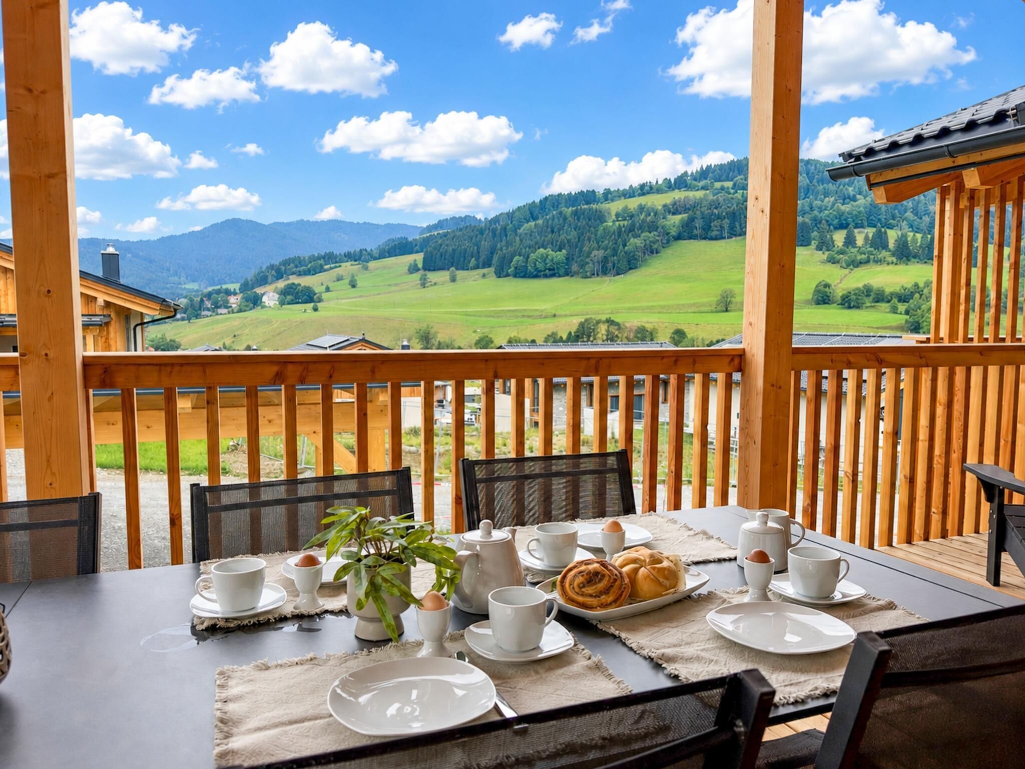 Eine Holterrasse mit einem Frühstückstisch, mit Blick auf eine gebirgige Landschaft.