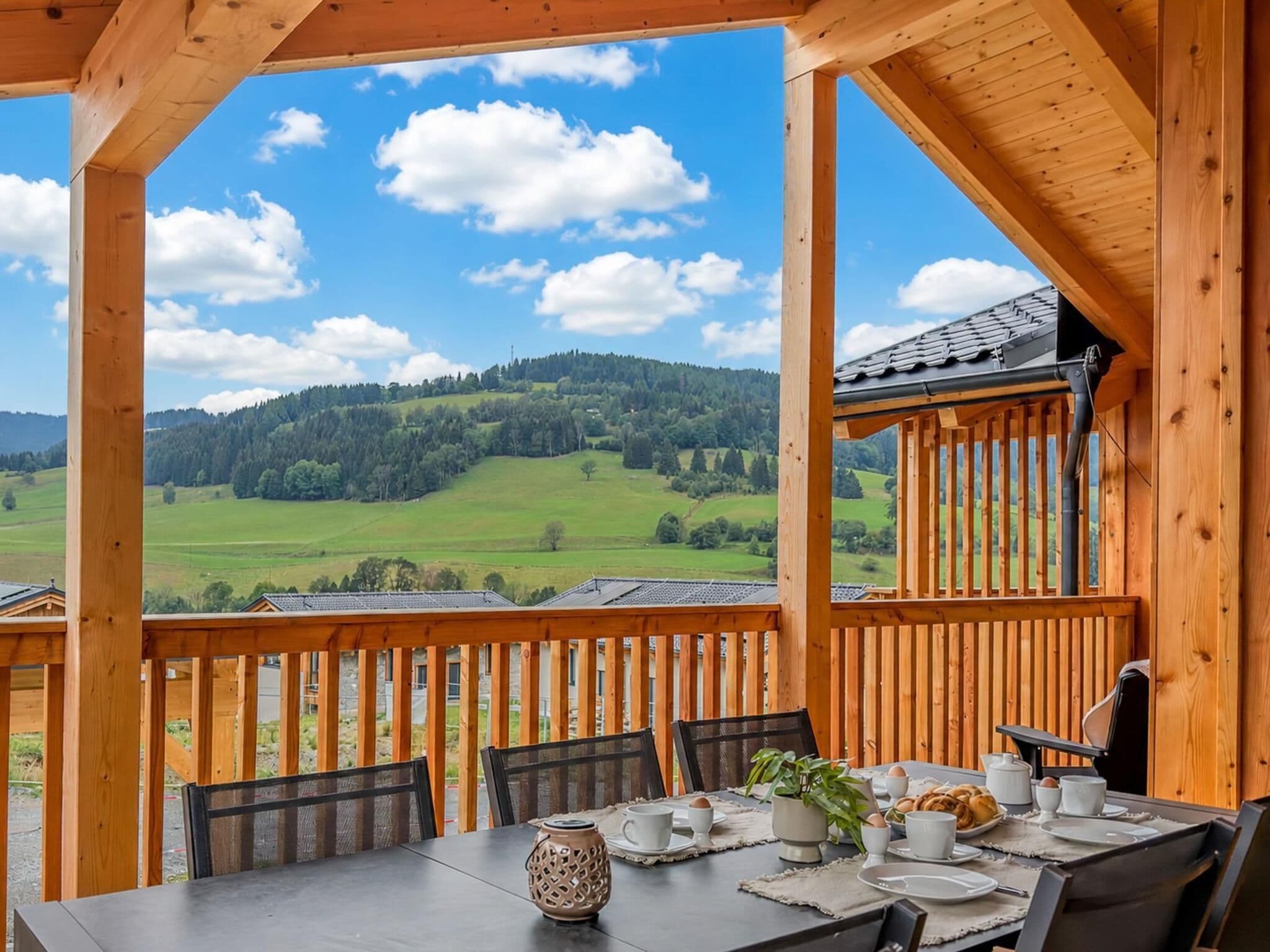 A wooden deck with a table set for breakfast, overlooking a green valley and hills.