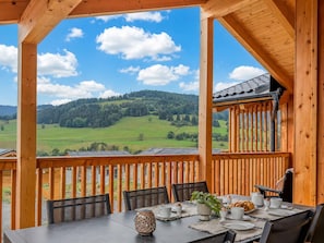 A wooden deck with a table set for breakfast, overlooking a green valley and hills. - Nice ski-in-ski-out lodge with sauna and balcony (Sankt Lambrecht)