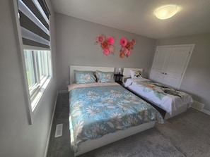 Une chambre avec deux lits, une fenêtre avec des stores, un luminaire fixé au mur et une porte.