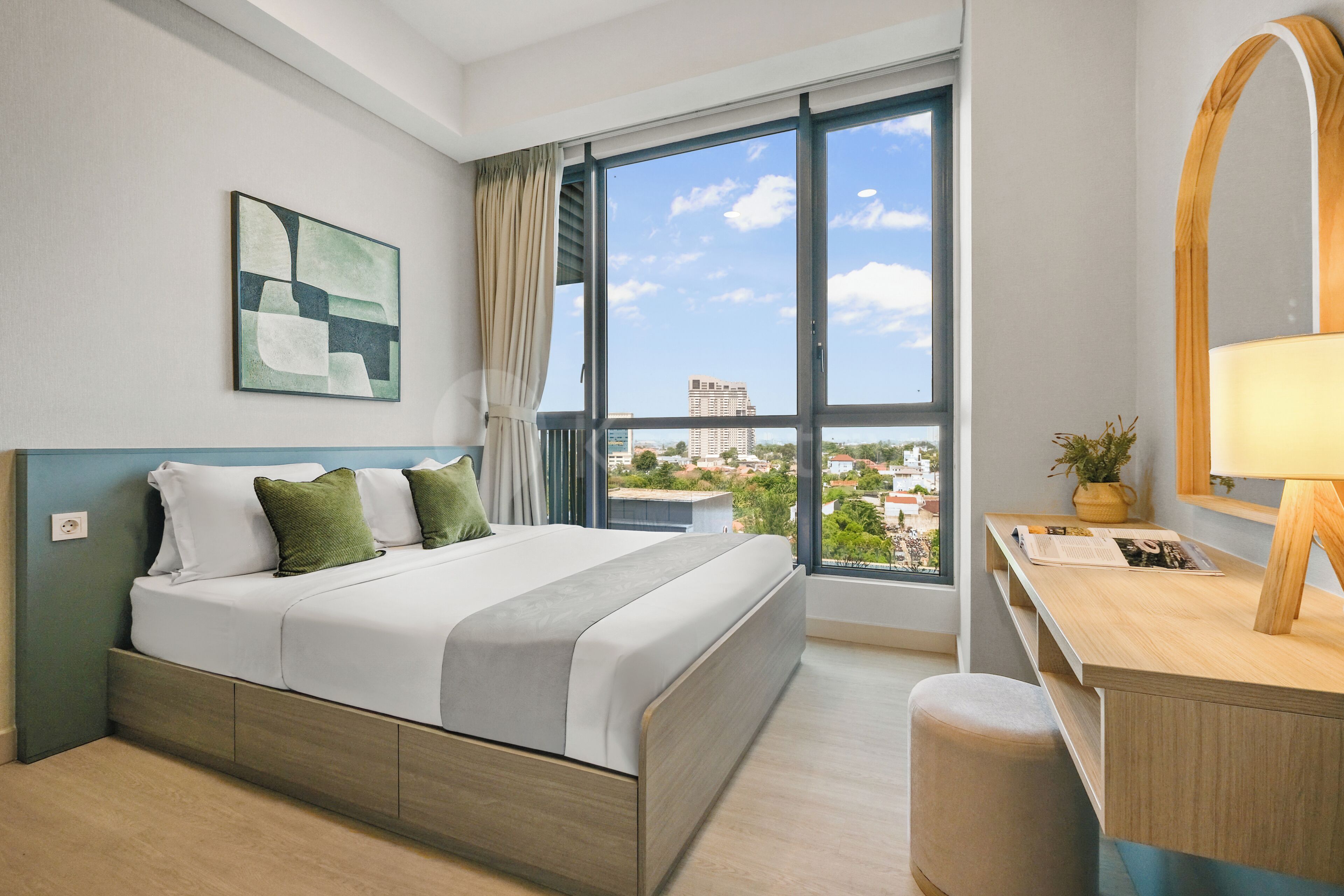 A hotel room with a bed, a desk, a window with a city view, and a painting on the wall.