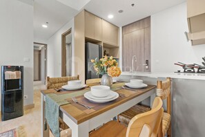 A modern kitchen with a dining area, equipped with a refrigerator, stove, and a vase with flowers. - Tamora by Kozystay - Cilandak (South Jakarta)