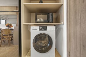 A compact laundry area with a washing machine and a microwave on a shelf. - Tamora by Kozystay - Cilandak (South Jakarta)