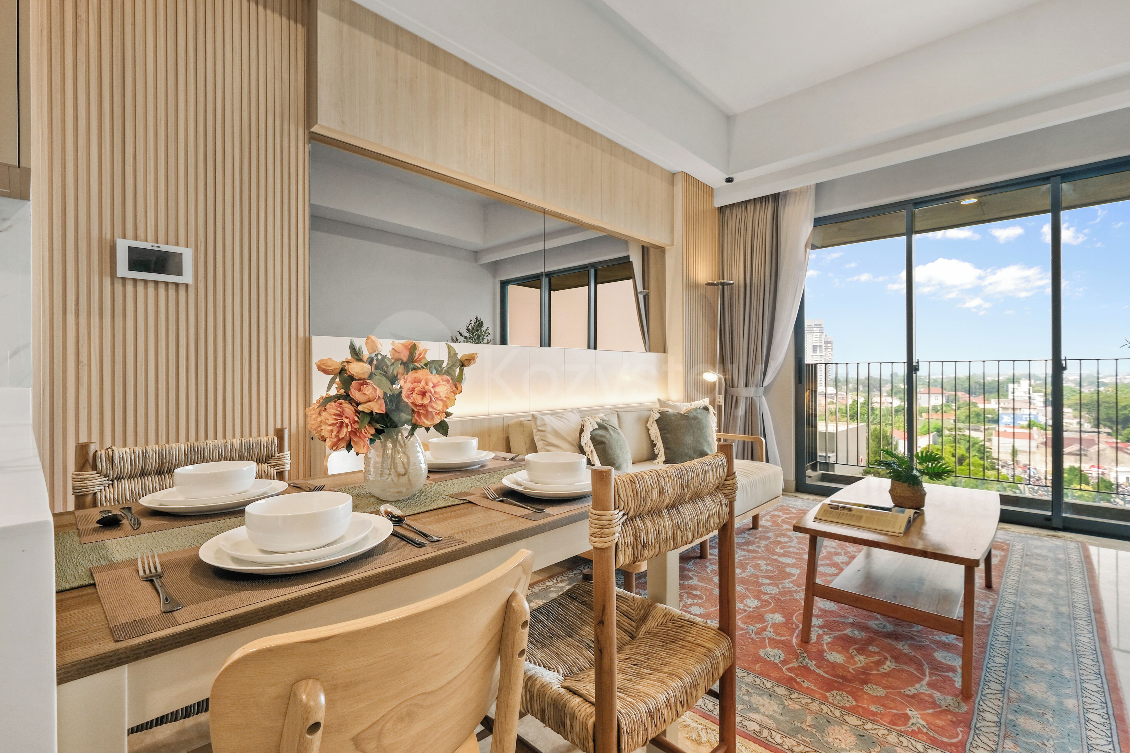Un comedor moderno con una mesa de madera dispuesta para cuatro personas, un sofá con cojines y vistas a la ciudad a través de grandes ventanales.