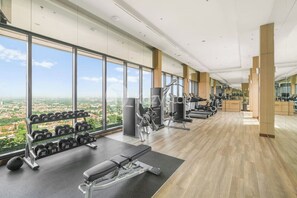 A modern gym with a panoramic view, equipped with various exercise machines and dumbbells. - Tamora by Kozystay - Cilandak (South Jakarta)