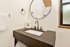 Un baño con lavamanos, espejo, toallero y ventana.