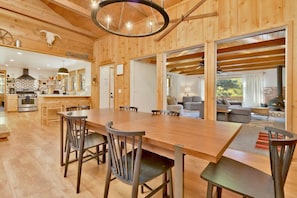 A spacious wooden interior with a large dining table, chairs, a kitchen area, and a seating area with a fireplace.