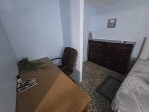 A small, simple room with a bed, a desk, and a chair. - Puntilla Deluxe Apartment (Cataño)