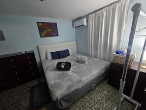 A hotel room with a bed, a painting on the wall, an air conditioning unit, and a window with curtains. - Puntilla Deluxe Apartment (Cataño)