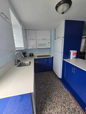 A compact kitchen with a sink, microwave, and refrigerator, featuring blue cabinets and a speckled floor. - Puntilla Deluxe Apartment (Cataño)