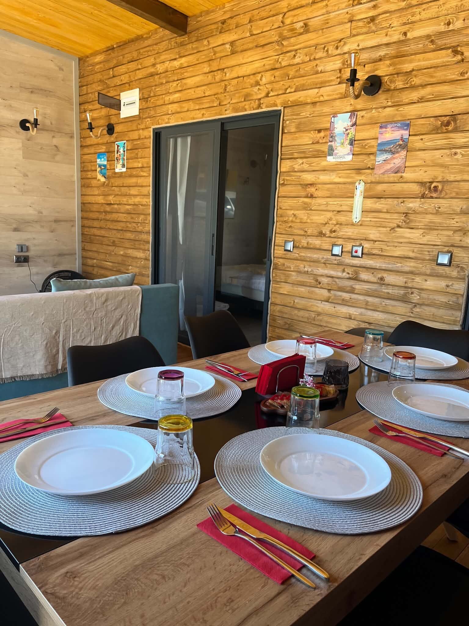 A dining area with wooden walls, a table set for four with plates, glasses, and cutlery.