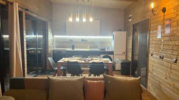 A cozy dining area with a wooden table and chairs, a sofa with cushions, and a kitchen in the background.