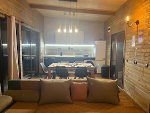 A cozy dining area with a wooden table and chairs, a sofa with cushions, and a kitchen in the background.