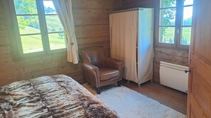 Ein Zimmer mit einem Bett, einem Sessel, einem kleinen Kühlschrank und einem Fenster mit Vorhängen.