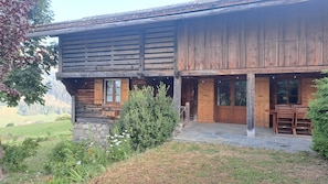 A rustic wooden cabin with a stone foundation, a covered porch, and a dining area with chairs. - L'Alpage 1884, in the heart of the Grand Bornand ski area (Le Grand-Bornand)