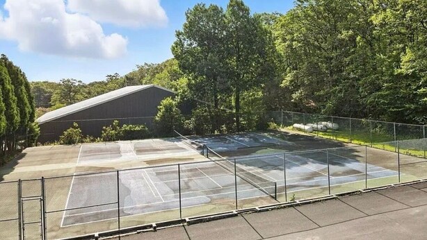 A tennis court with a net, surrounded by a fence, and a building in the background. - Mountainside Townhome close to Waterparks, ski slopes and hiking trails. (Tannersville)