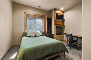 Un dormitorio con cama, escritorio, silla, chimenea y ventana con vistas a árboles.
