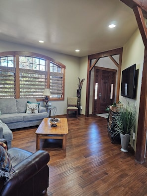 A spacious living room with a wooden floor, a sofa, a coffee table, and a television. - Buffalo Teal Lodge|Hot Tub|Resort Amenities (Klamath Falls)