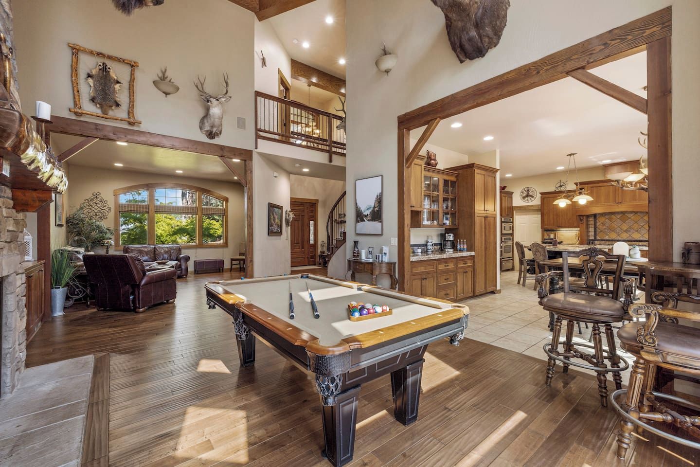 A spacious living area with a pool table, wooden flooring, and a high ceiling with exposed beams.
