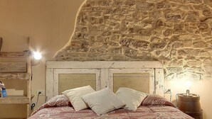Un dormitorio con pared de piedra, estructura de cama de madera y mesita de noche con lámpara.