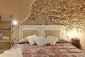 A bedroom with a stone wall, a wooden bed frame, and a nightstand with a lamp. - Casa Camomilla C: A characteristic and welcoming two-story independent house surrounded by meadows and by green hills, with Free WI-FI. (Pontassieve)