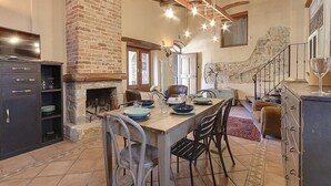 Una cocina rústica con chimenea de piedra, vigas de madera y una mesa de comedor lista para cuatro comensales.