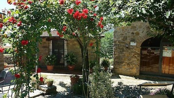 Une cour avec un bâtiment en pierre, des plantes en pot et une table entourée de chaises.