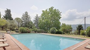 Una piscina rectangular con borde de azulejos, rodeada de sillas de descanso y follaje.