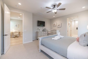 Un dormitorio con cama, ventilador de techo, televisor, cuna y una puerta que da a otra habitación.