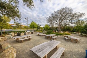 Un patio al aire libre con varias mesas y bancos de madera, rodeado de rocas y follaje.