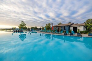 Una piscina con sillas de descanso y un edificio con puerta y ventanas.