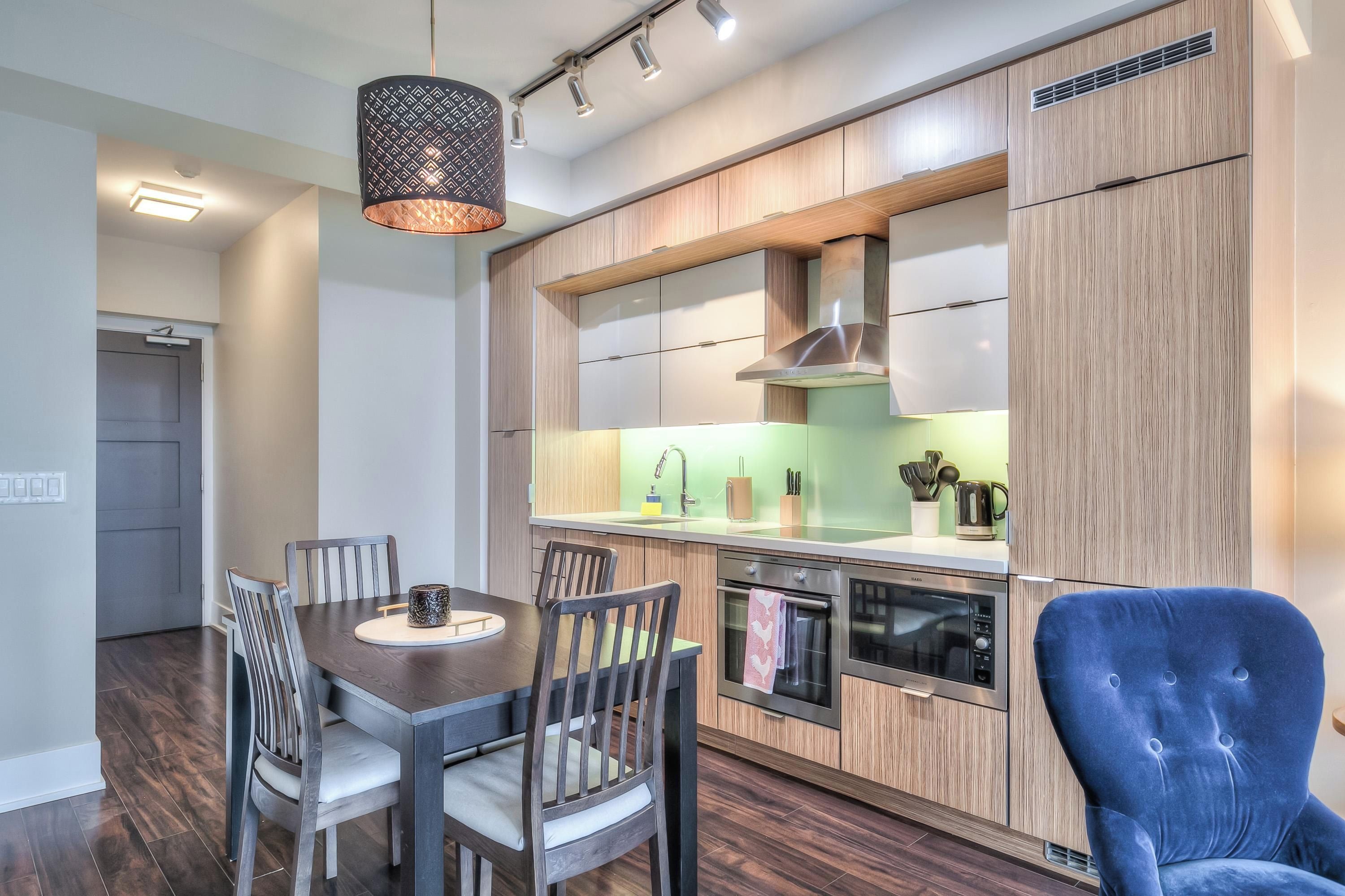 Una cocina moderna con armarios de madera, horno empotrado y comedor con mesa y sillas.