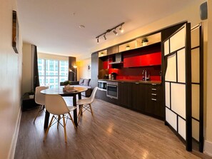 Una cocina moderna con armarios rojos, un comedor con una mesa redonda y sillas, y vistas de un edificio a través de amplios ventanales.