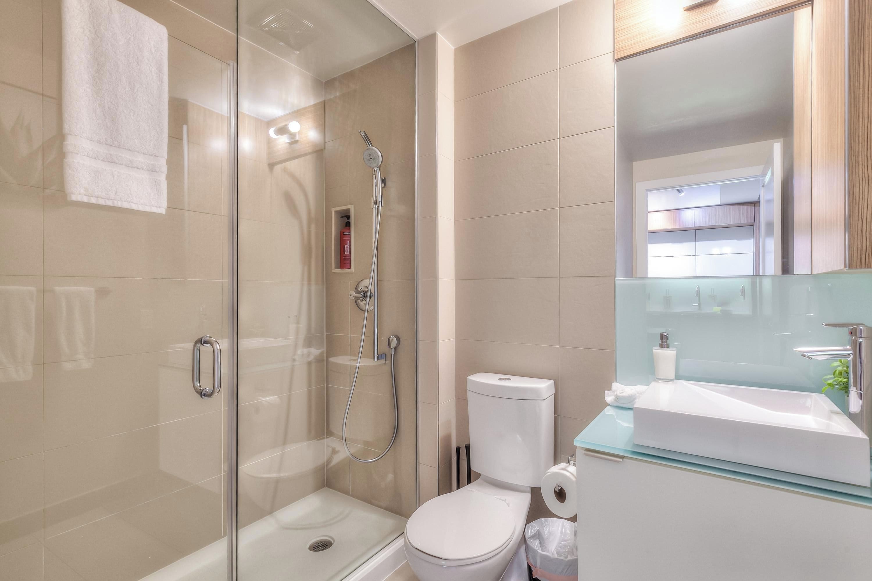 Een moderne badkamer met een douchecabine van glas, een wit toilet en een glazen wastafel.