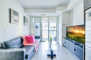 Una sala moderna con un sofá gris, una mesa de centro de vidrio y un televisor plano grande sobre un mueble de madera.
