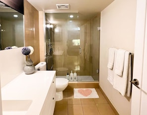 Un baño moderno con ducha envuelta en vidrio, inodoro blanco y tocador con un jarrón de flores.