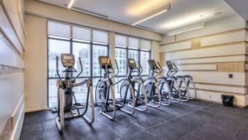 A gym with treadmills aligned against a wall with large windows, allowing natural light and views of the cityscape.