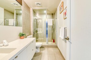 Un baño moderno con ducha envuelta en vidrio, lavamanos blanco y retrete.