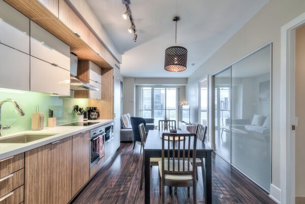 A modern kitchen with wooden cabinets, a dining area with a table and chairs, and a large window providing natural light.