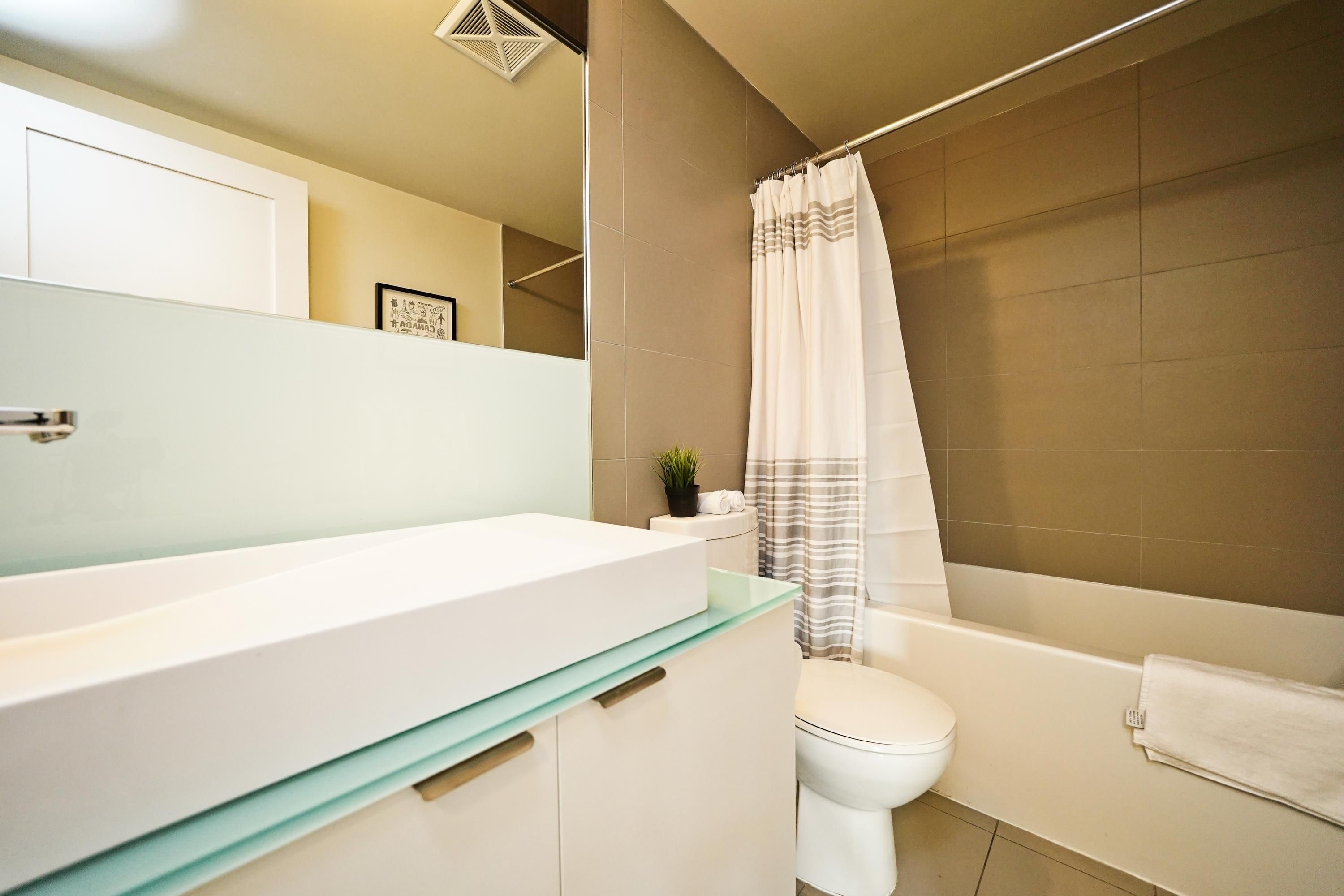A modern bathroom with a large white bathtub, a glass-topped vanity, and a toilet.