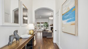 A hallway with a wooden bench, a mirror, a lamp, and a painting on the wall. - DFW retreat with pool, hot tub, and back yard oasis (Irving)