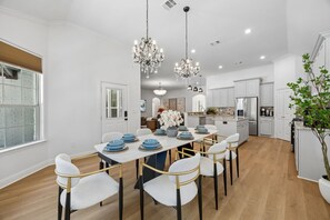 A modern kitchen with white cabinetry, a central island, and a dining area with a long table and chairs. - DFW retreat with pool, hot tub, and back yard oasis (Irving)