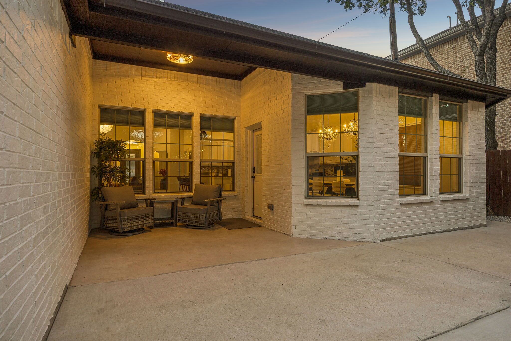 A covered patio with a brick wall, a table with chairs, and a large window.