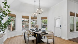 A dining area with a chandelier, white walls, and large windows. - DFW retreat with pool, hot tub, and back yard oasis (Irving)