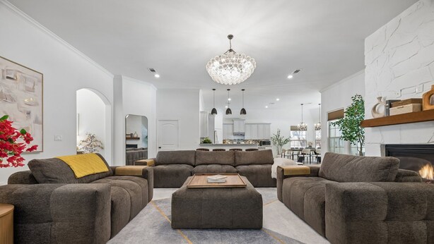 A modern living room with a fireplace, a dining area, and a kitchen in the background. - DFW retreat with pool, hot tub, and back yard oasis (Irving)