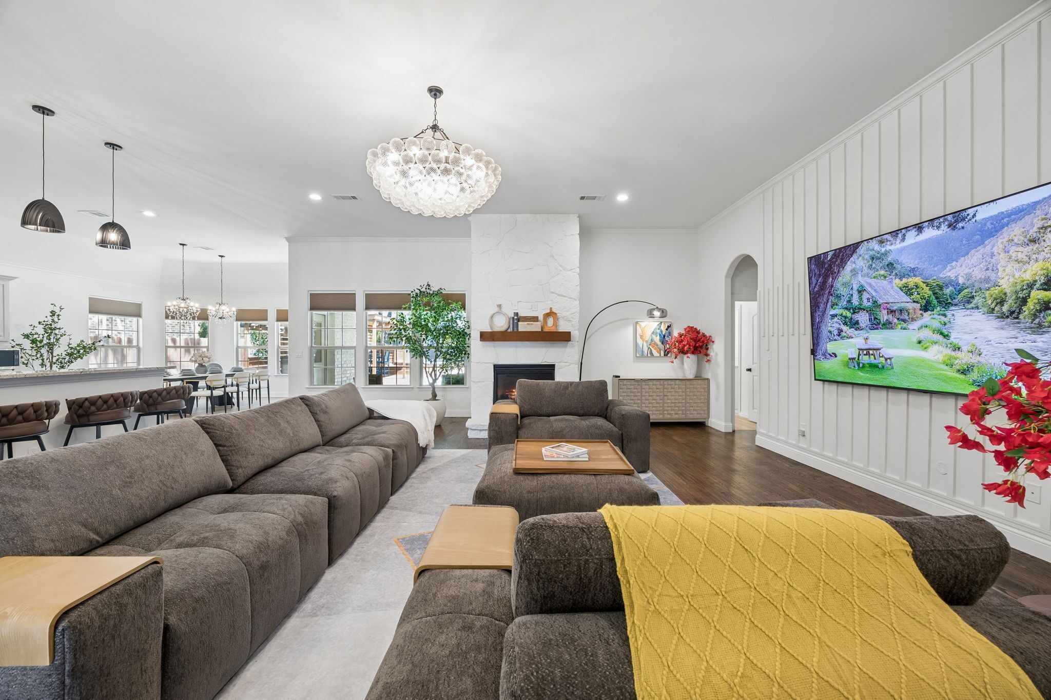 Een moderne woonkamer met een open haard, een grote televisie en een eethoek met hanglampen.