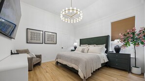 A modern bedroom with a bed, bedside tables, a chair, a hanging light fixture, and a potted plant. - DFW retreat with pool, hot tub, and back yard oasis (Irving)