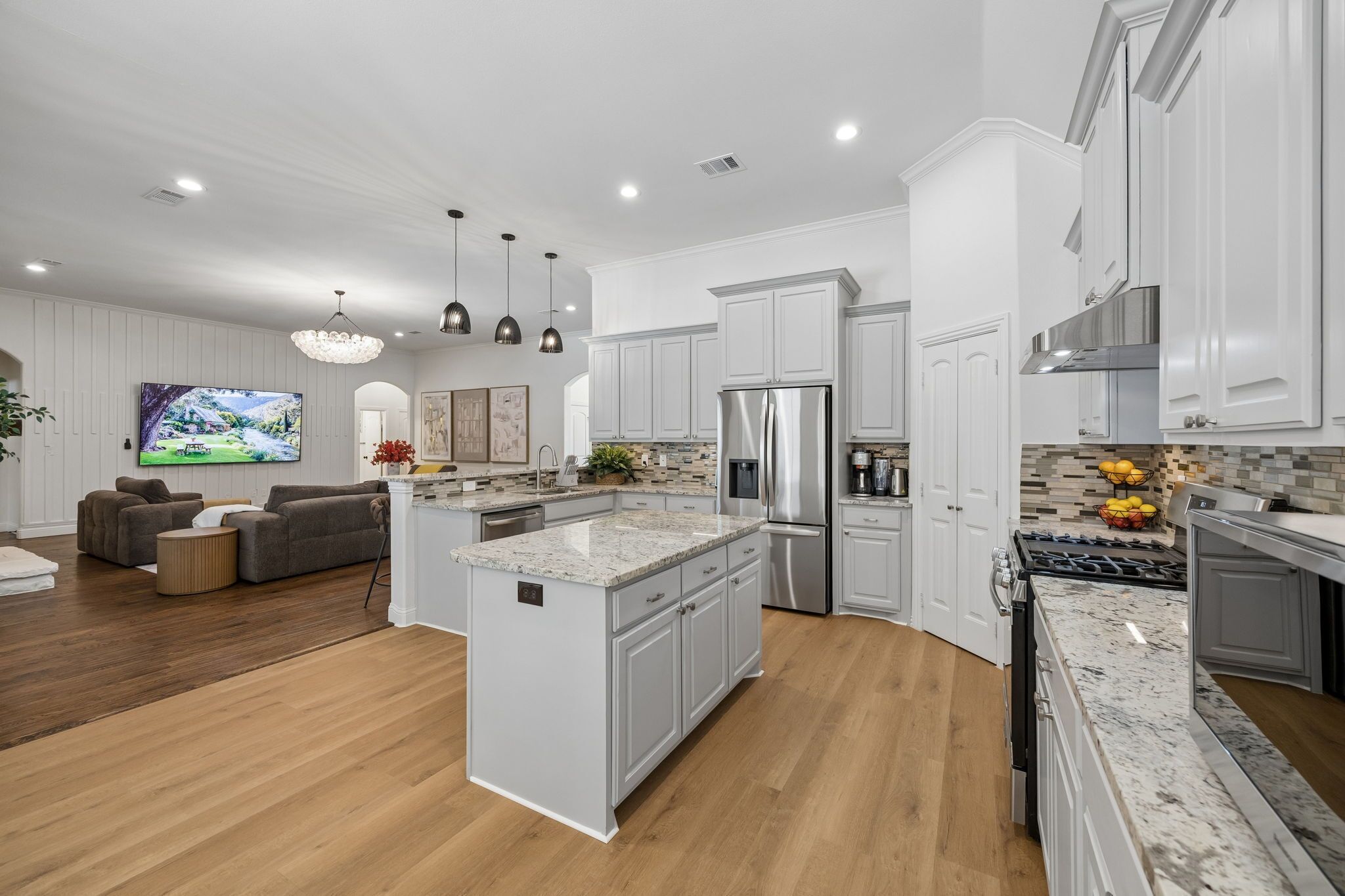 A modern kitchen with white cabinetry, a central island, stainless steel appliances, and a dining area with a gray sofa.